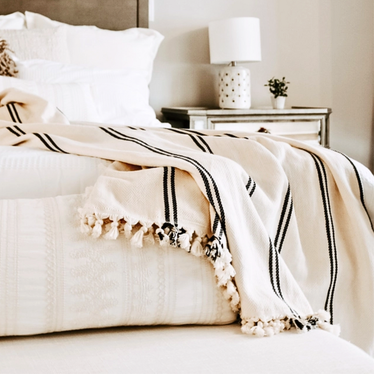 beautful cream Turkish throw with stylish black strips and edged in fringe draped across the corner of a plush beige bed.