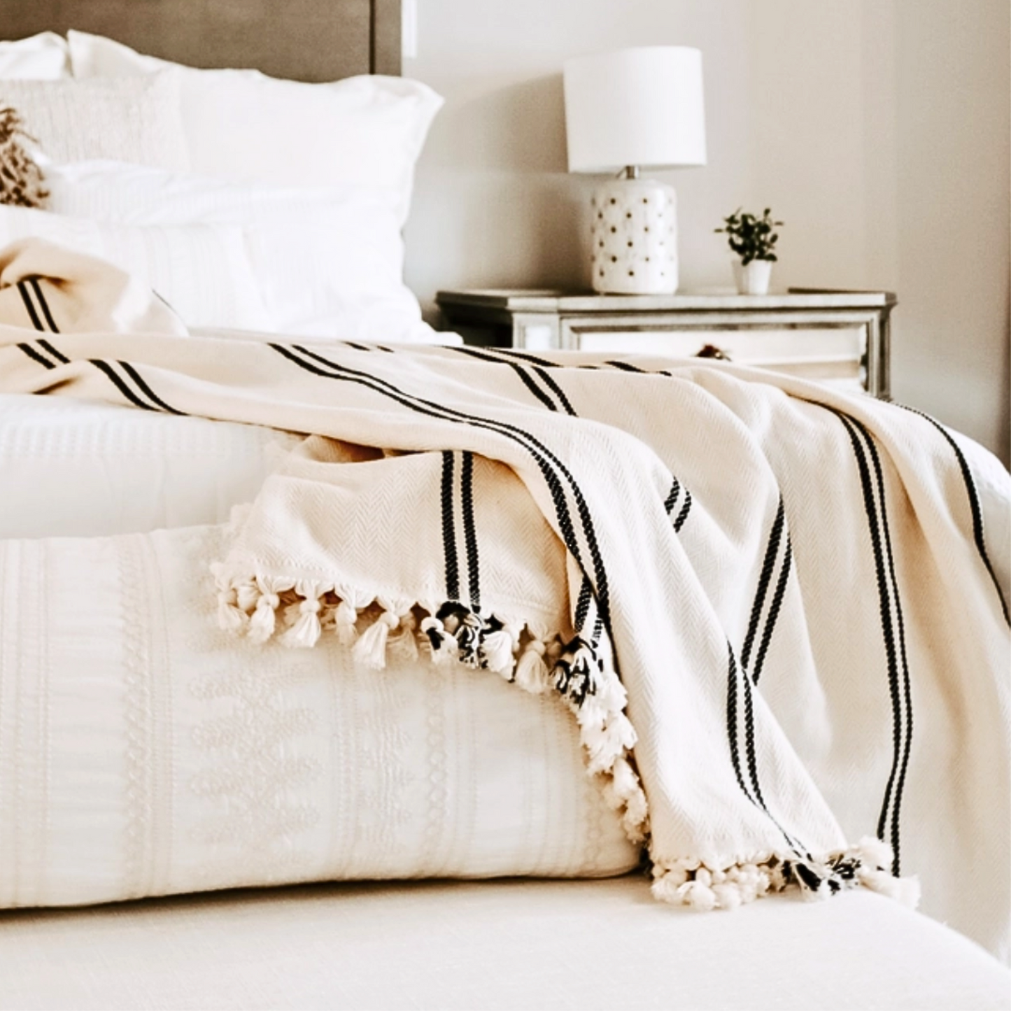 Off white with black stripes luxurious turkish throw with fringe draped across the end of a bed in a stylish bedroom.