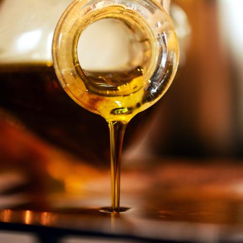 Close up of golden oil pouring from a glass bottle