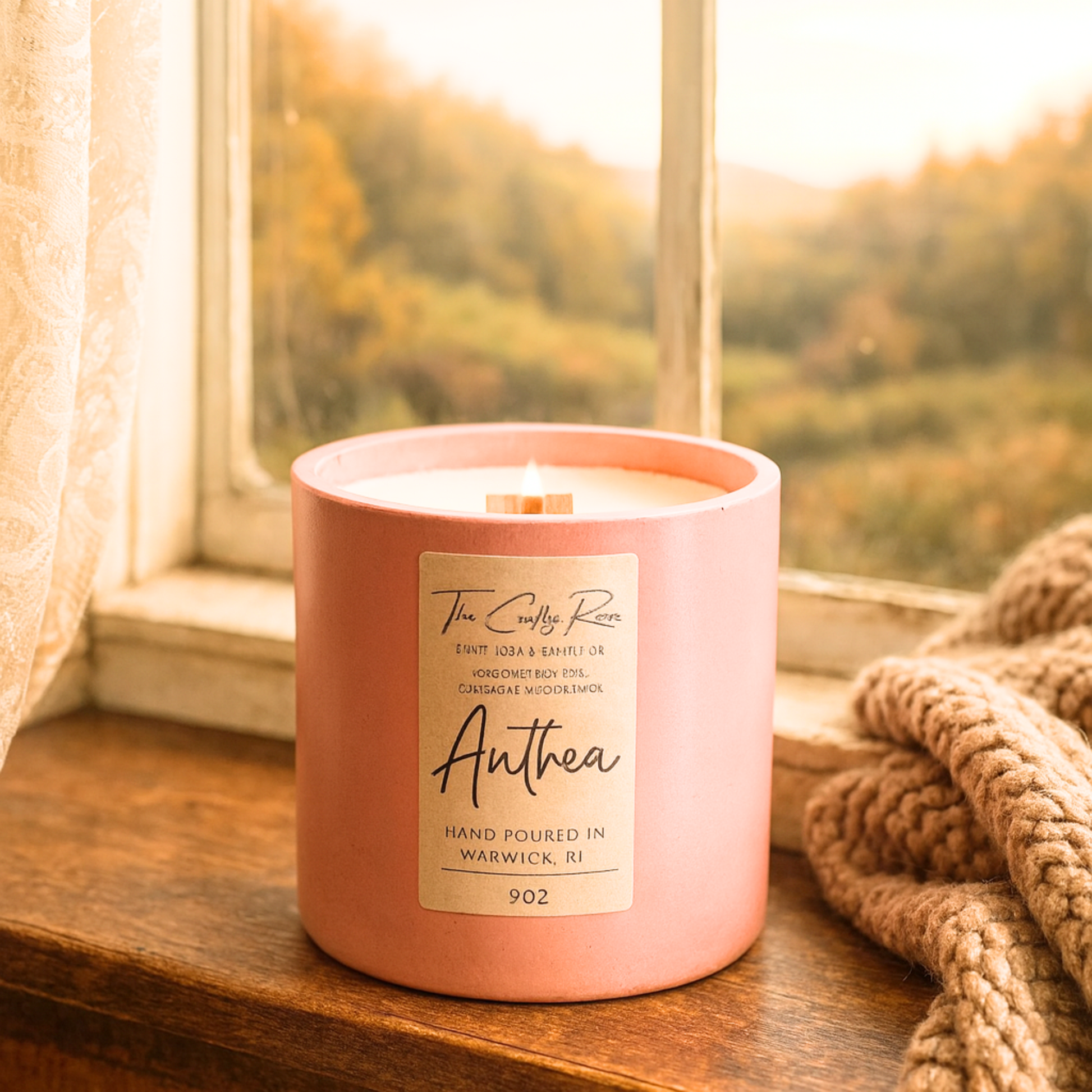 Lit Pink labeled candle with a wooden wick on a wooden window ledge with a scenic view.