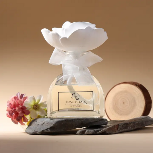 Clear glass bottle featuring a white ceramic flower, sitting on a flat stone.