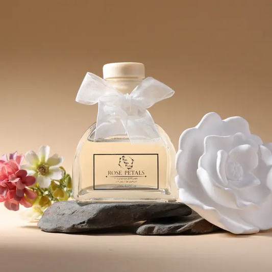 clear glass bottle filled with golden oil. a white bow around the neck and the ceramic flower sitting on the side. 