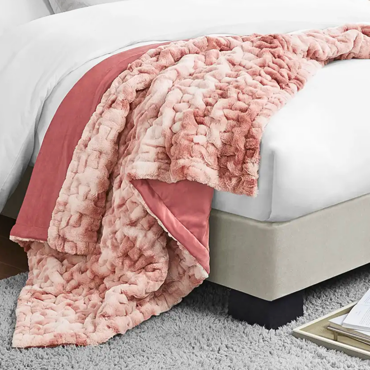 A pink ruched throw blanket draped over the edge of a bed, with a一部分 of the ruched pattern visible.