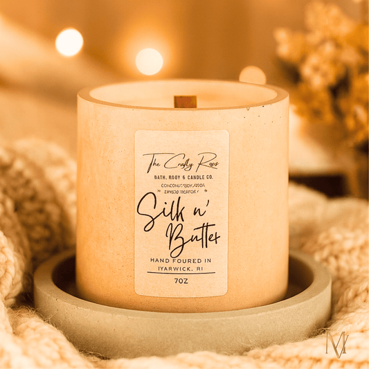 Beige Candle with a label displayed on a knit throw with warm lighting softly blurred in the background