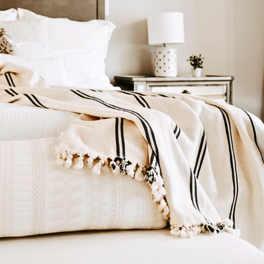Off white with black stripes luxurious turkish throw with fringe draped across the end of a bed in a stylish bedroom.
