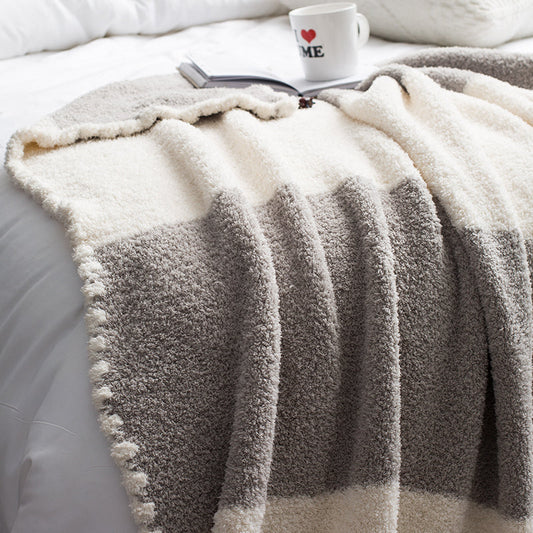 A luxurious chenille throw blanket in white and gray gradient pattern, draped over the edge of a bed with a book and a mug. 