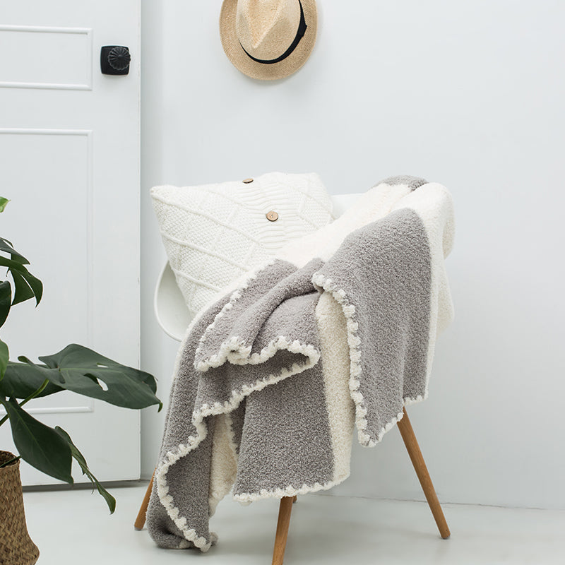 A luxurious chenille throw blanket in white and gray gradient pattern, draped over the back of a wooden chair, with a plant and a hat in the background.